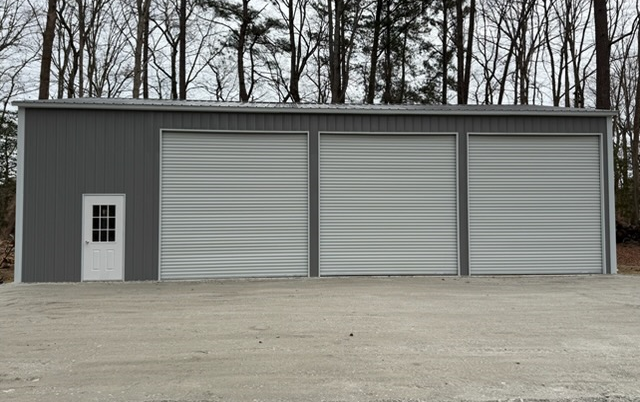 Gray metal garage building with three garage doors on a paved lot