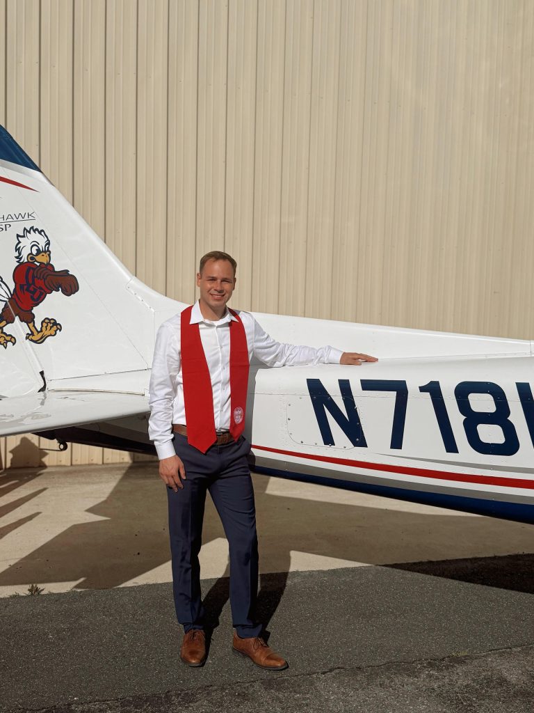 Man in a red vest standing next to a small propeller airplane