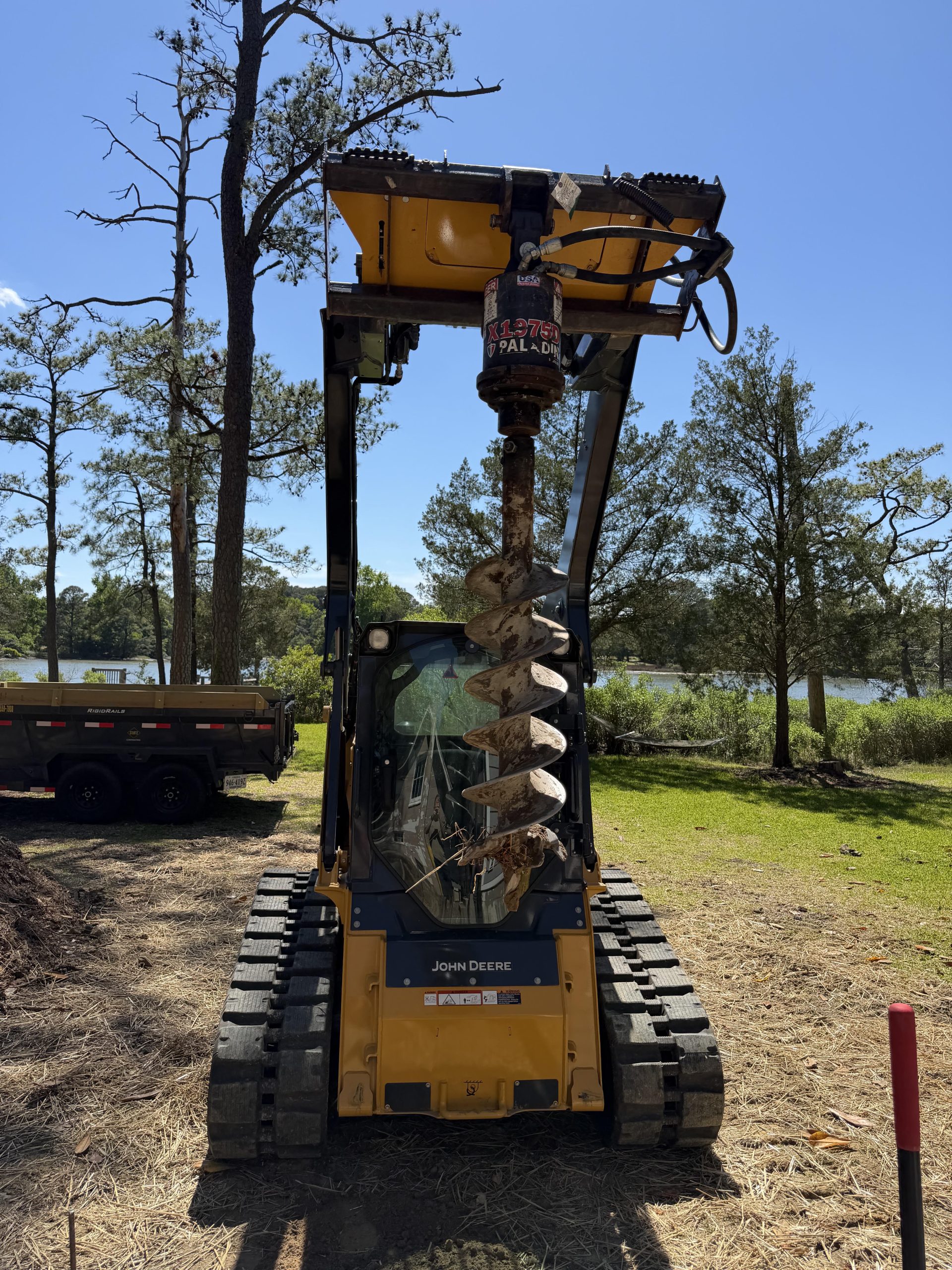 Skid steer with an auger drill attachment parked near a lake