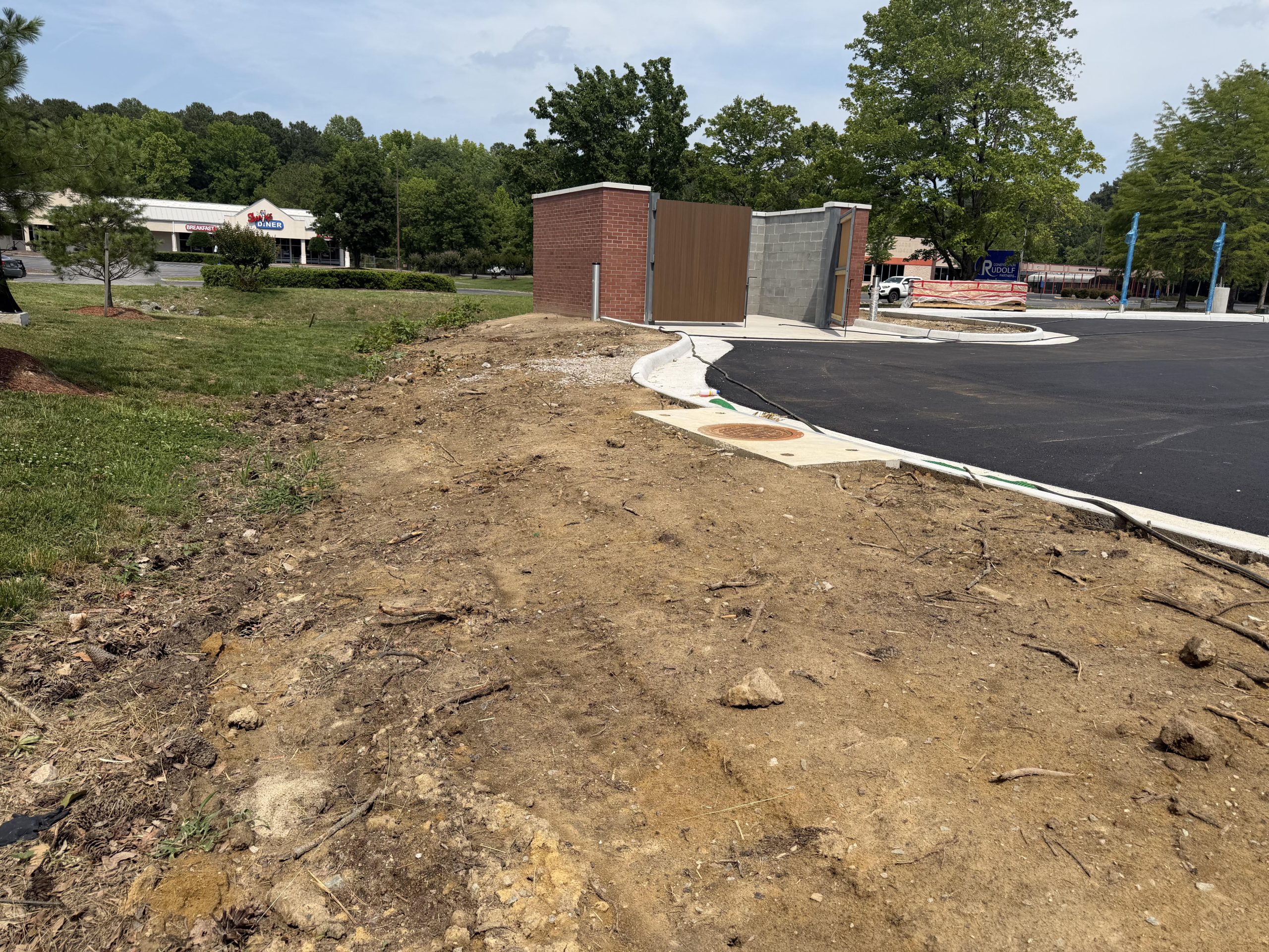 Newly graded dirt lot beside a brick building and freshly paved lot