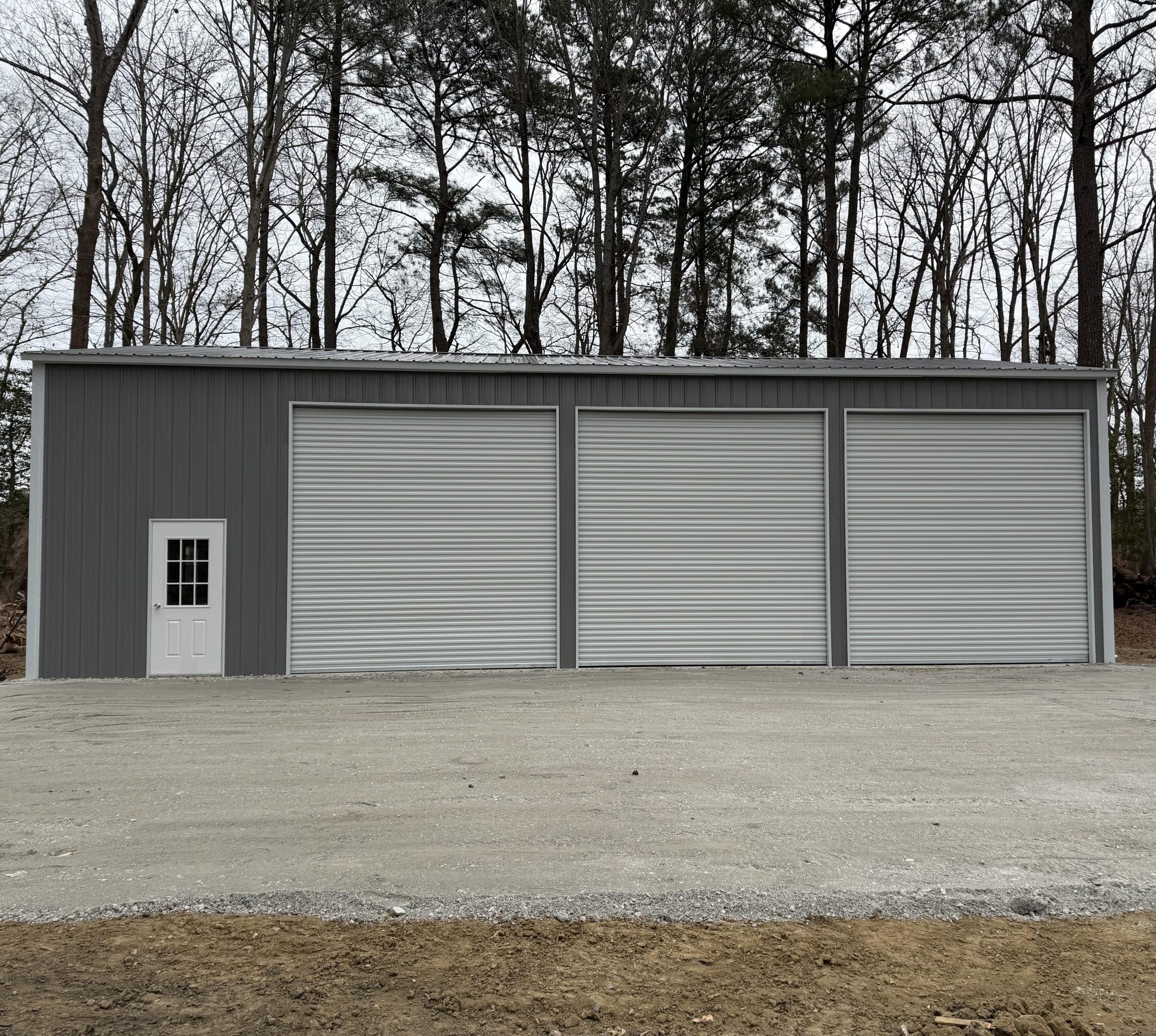 New gray metal garage building with three garage doors on a gravel pad