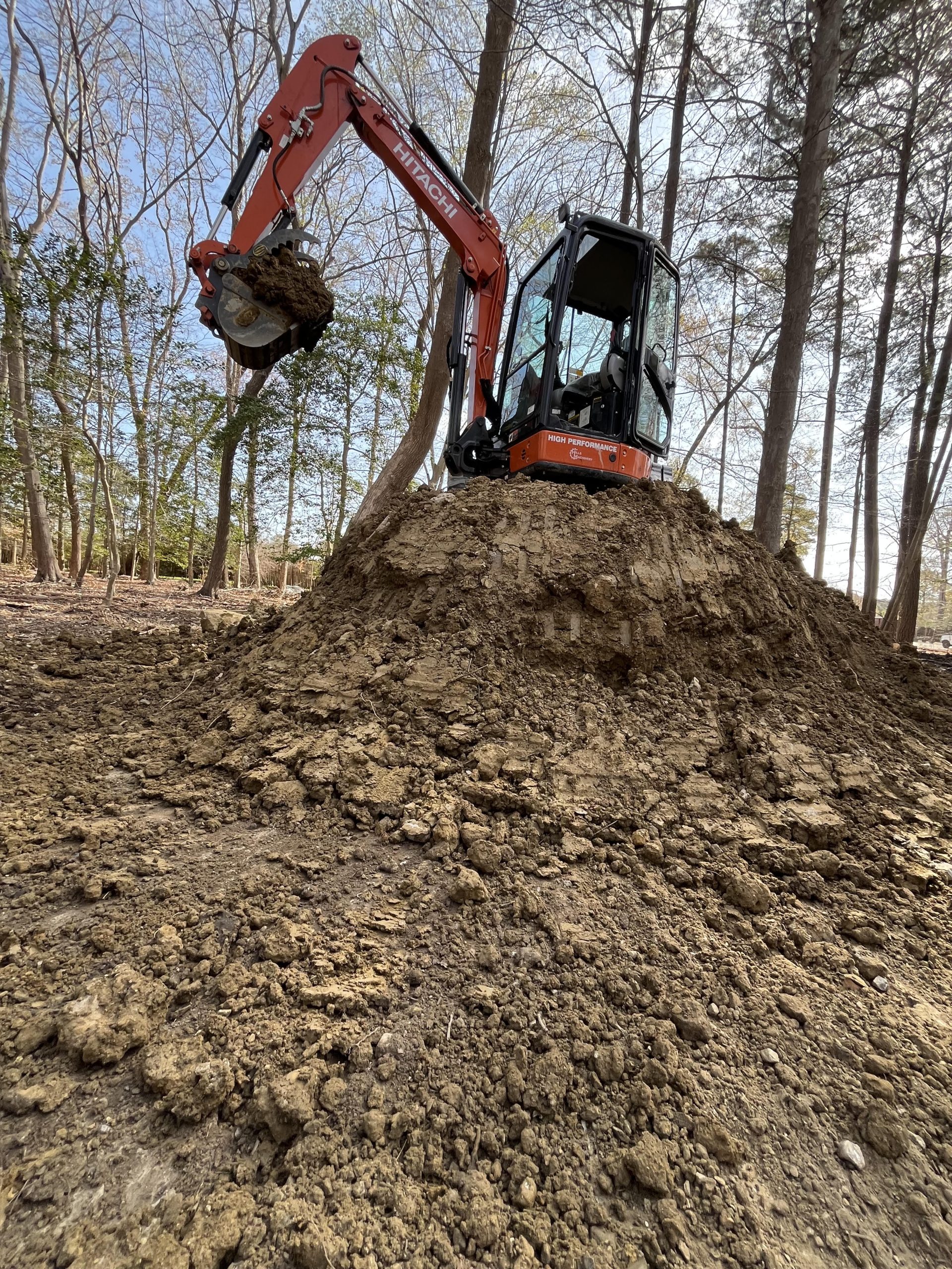 Excavator arm dumping dirt onto a large dirt pile