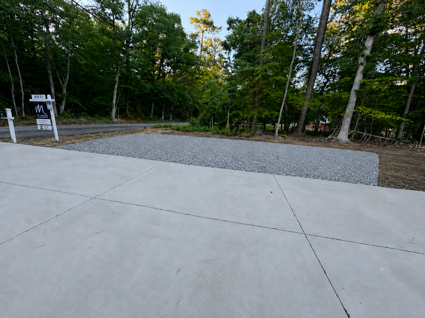 New gravel parking pad installed next to a concrete driveway in a wooded lot