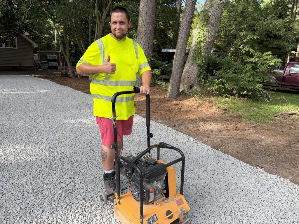 Worker giving a thumbs up next to a plate compactor on a new gravel driveway