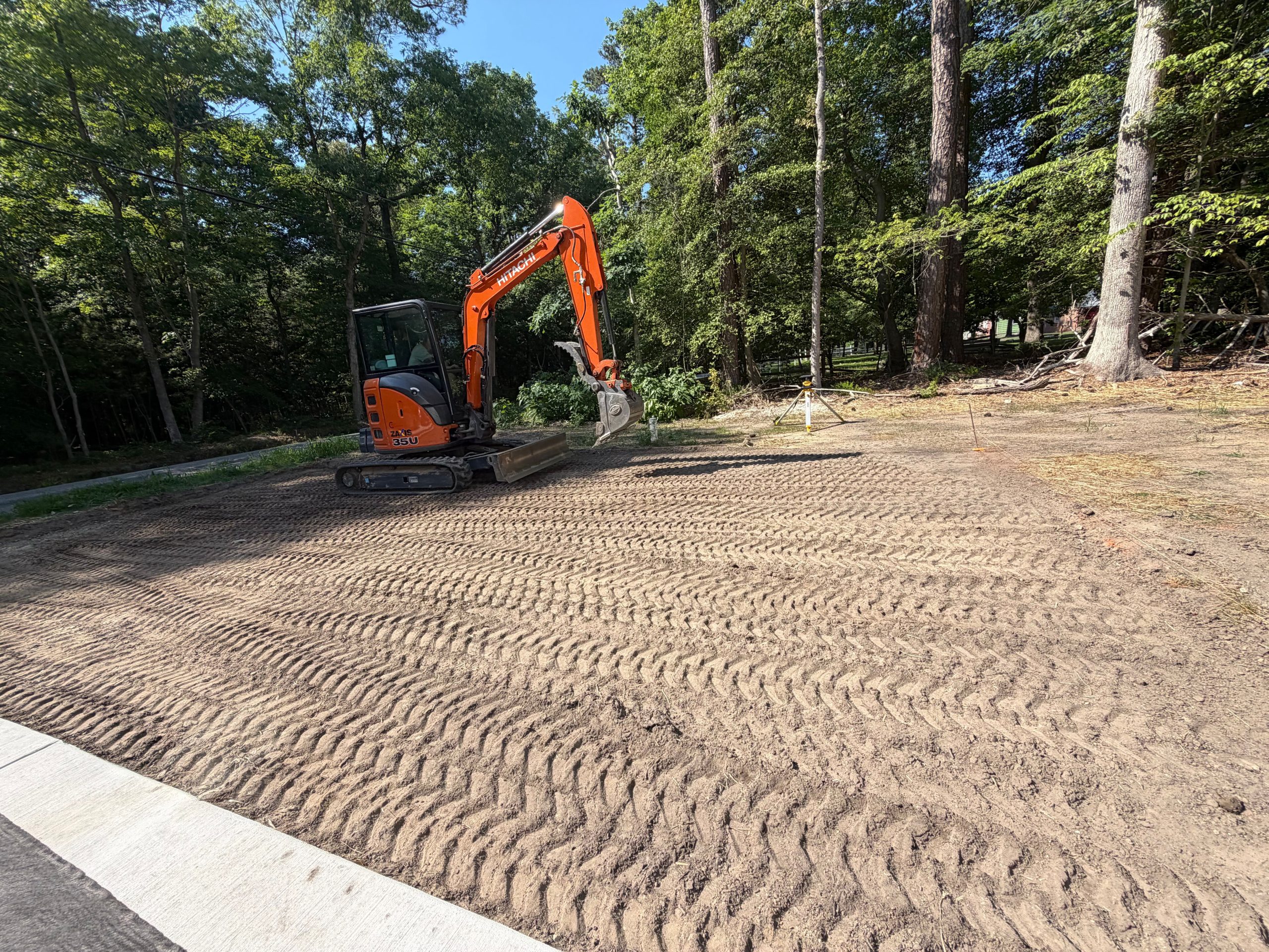 Graded dirt driveway area near a sidewalk, tread marks visible